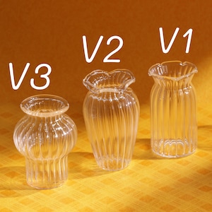 May include: Three clear glass vases with unique designs. The vases are labeled V1, V2, and V3. V1 has a ruffled top, V2 has vertical ridges, and V3 has a bulbous shape. The background is a solid orange color.