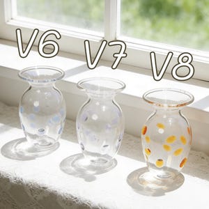 May include: Three clear glass vases with rounded bodies and flared rims are displayed on a white surface. The vases are decorated with colorful polka dots. The text "V6", "V7", and "V8" is above each vase.