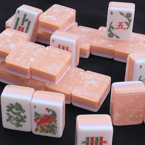 May include: A collection of rectangular mahjong tiles featuring a marbled peach and white color scheme. The tiles display various engraved symbols, numbers, and illustrations in red and green ink, with some tiles showing blank marbled surfaces.