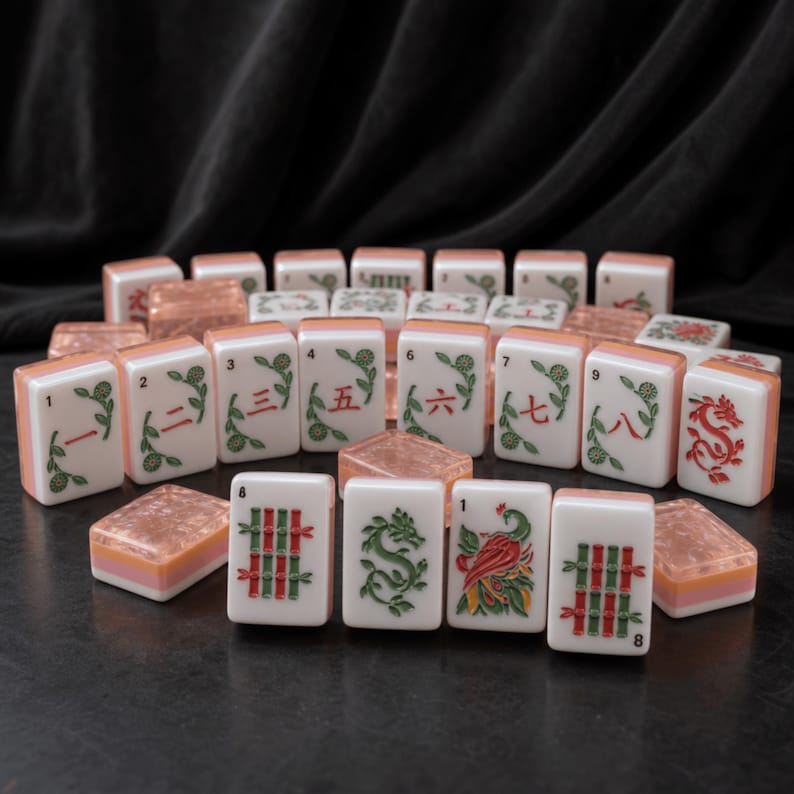 May include: A set of rectangular mahjong tiles featuring white faces with green and red engraved designs, including Chinese numerals, bamboo stalks, dragons, and a bird. The tiles have translucent, textured peach-colored backs and sides.