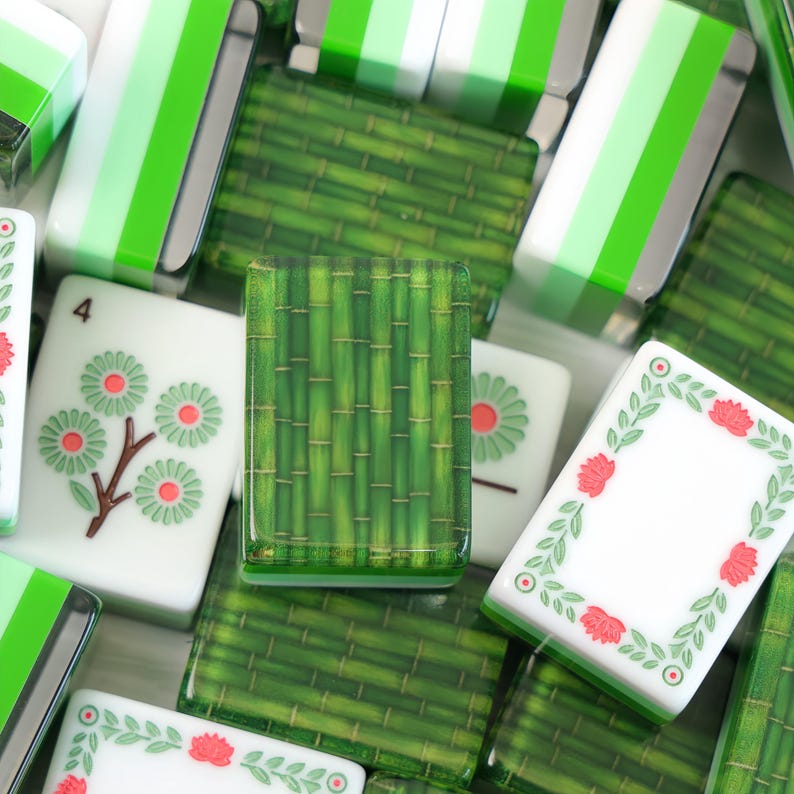 K&ouml;nnte beinhalten: Eine Sammlung rechteckiger Mahjong-Spielsteine mit verschiedenen Motiven. Einige Steine zeigen ein gr&uuml;nes Bambusmuster, w&auml;hrend andere wei&szlig; sind und gr&uuml;ne Blumenmotive, rote Akzente sowie die in schwarzer Tinte aufgedruckte Zahl vier aufweisen.