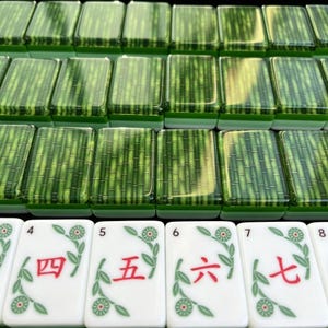 K&ouml;nnte beinhalten: Ein Set rechteckiger Mahjong-Spielsteine mit einem gr&uuml;nen Bambusmuster auf der R&uuml;ckseite und wei&szlig;en Vorderseiten, die die roten chinesischen Ziffern vier, f&uuml;nf, sechs und sieben sowie gr&uuml;ne florale Rankenmotive zeigen.
