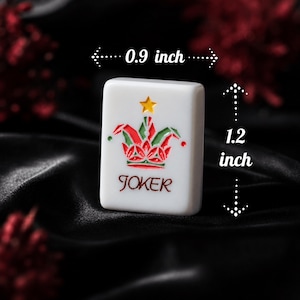 May include: A white rectangular mahjong tile featuring a colorful joker hat graphic with a yellow star above it and the word JOKER printed in red below. The tile measures 0.9 inches in width and 1.2 inches in height as indicated by arrows.