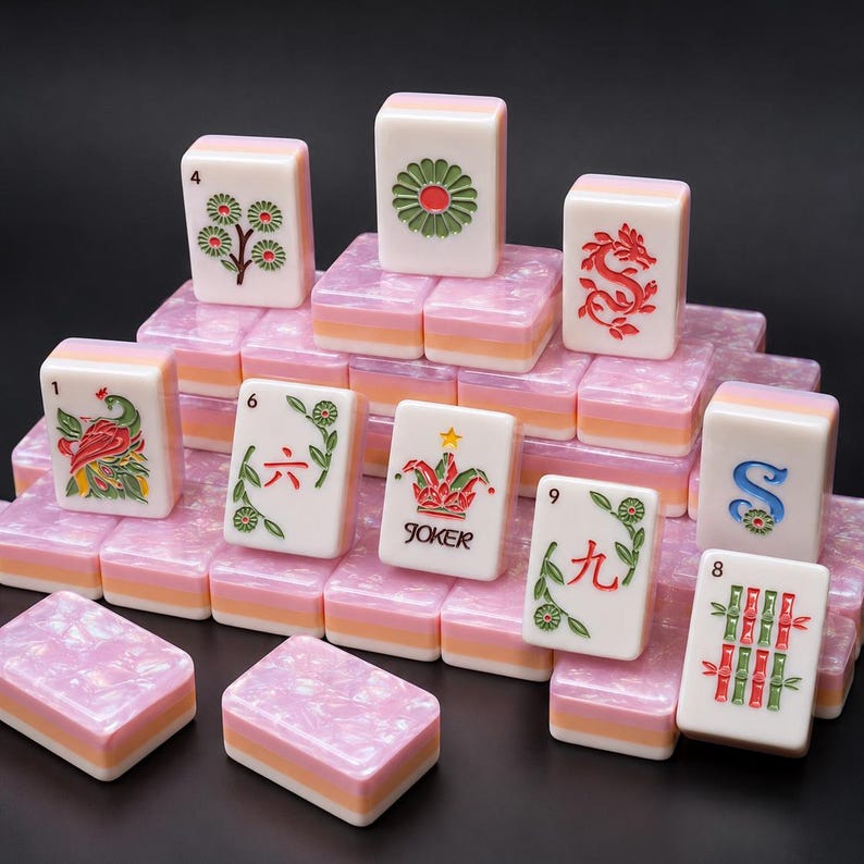 May include: A collection of rectangular mahjong tiles with white faces featuring colorful engraved designs including a peacock, a joker, a dragon, and floral patterns. The tiles have a layered base of pink, white, and orange pearlescent acrylic.