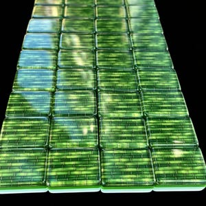 May include: A grid of square glass tiles arranged in a rectangular formation. Each tile features a vibrant green color with a horizontal bamboo-like pattern printed on the surface. The tiles have a glossy, reflective finish and smooth edges.