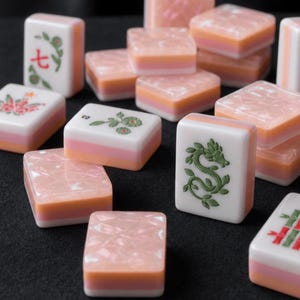 K&ouml;nnte beinhalten: Eine Sammlung rechteckiger Mahjong-Spielsteine mit einem geschichteten Design, bestehend aus einem wei&szlig;en Oberteil und einer rosa-orangen Basis. Einige Steine zeigen eingravierte gr&uuml;ne und rote Symbole, darunter einen Drachen, florale Muster und die Zahl sieben.