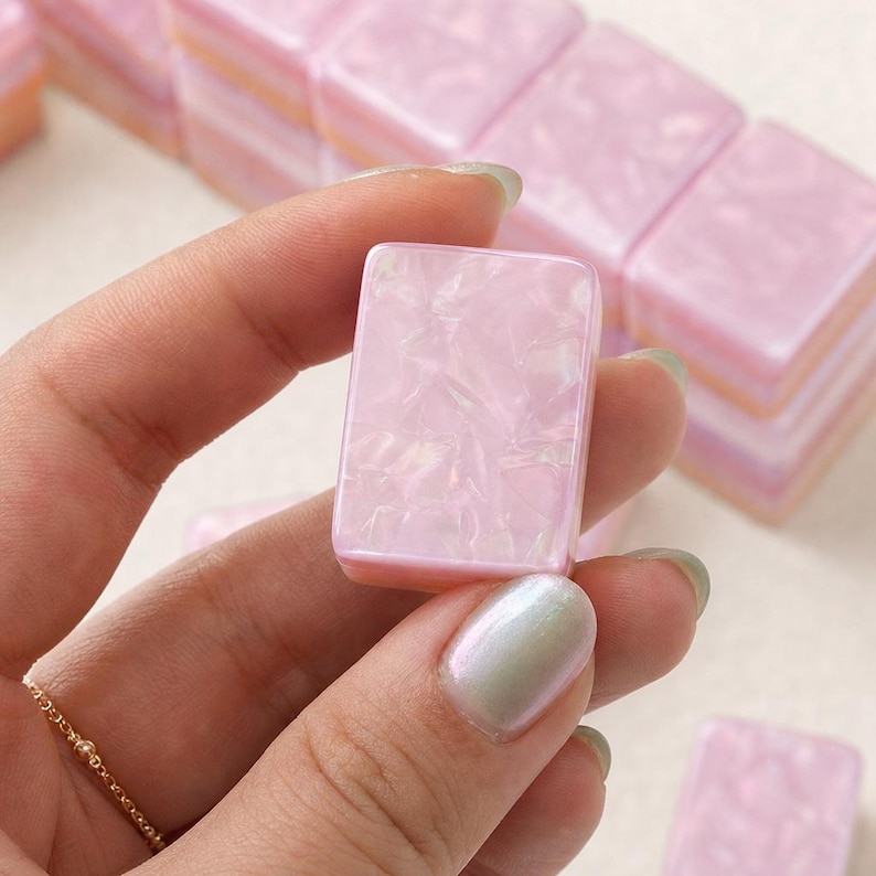 May include: A rectangular mahjong tile with a glossy, light pink marbled finish. The tile features a smooth, polished surface with subtle pearlescent swirls throughout the material, creating a soft, reflective appearance consistent with other tiles.