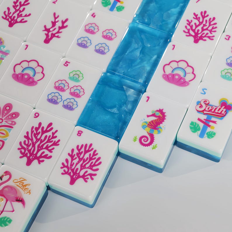 May include: A set of white Mahjong tiles featuring colorful ocean-themed graphics including pink coral, seashells, seahorses, and a flamingo. Some tiles display numbers and the text 'Sorth' or 'Joker'. A row of translucent blue tiles is included.