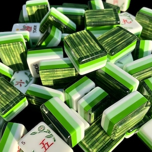 K&ouml;nnte beinhalten: Eine Sammlung rechteckiger Mahjong-Spielsteine mit einem geschichteten Design, bestehend aus einer wei&szlig;en Basis, einem hellgr&uuml;nen Mittelstreifen und einer dunkelgr&uuml;nen Oberseite mit Bambusmuster. Einige Spielsteine zeigen rote und gr&uuml;ne Blumen- oder Zahlensymbole.
