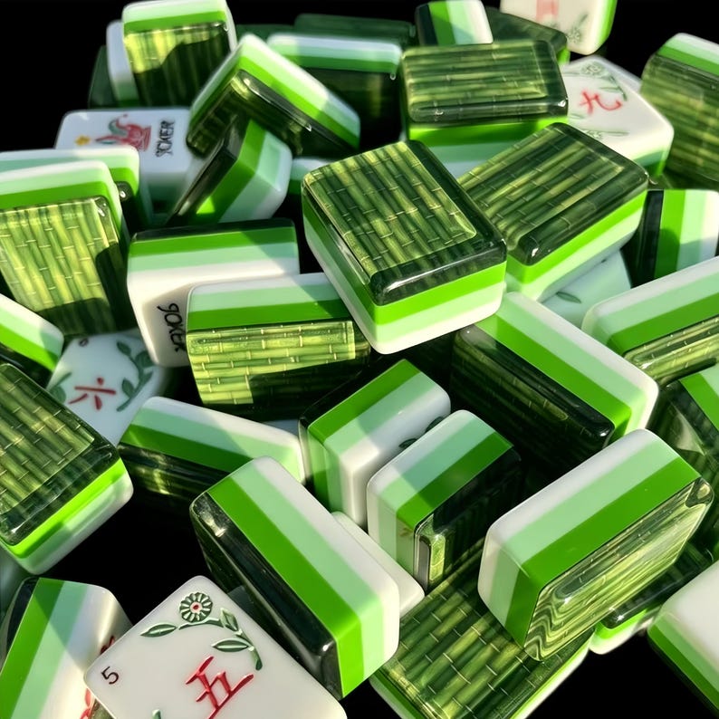 K&ouml;nnte beinhalten: Eine Sammlung rechteckiger Mahjong-Spielsteine mit einem geschichteten Design, bestehend aus einer wei&szlig;en Basis, einem hellgr&uuml;nen Mittelstreifen und einer dunkelgr&uuml;nen Oberseite mit Bambusmuster. Einige Spielsteine zeigen rote und gr&uuml;ne Blumen- oder Zahlensymbole.