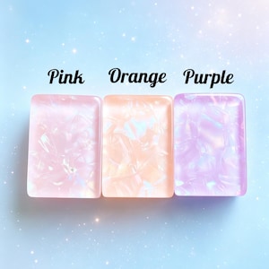 May include: Three rectangular acrylic pieces with a pearlescent, marbled finish in pink, orange, and purple. Each piece features a smooth, glossy surface with internal light-reflecting patterns. The words Pink, Orange, and Purple are printed above.