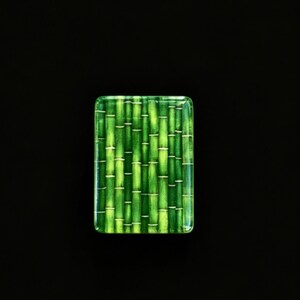 May include: A rectangular glass tile featuring a vibrant green bamboo stalk pattern. The design displays multiple vertical stalks in varying shades of lime and forest green, with horizontal nodes and a smooth, glossy finish on the surface.