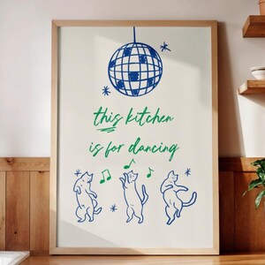 May include: A framed wall art print on a light background featuring a blue disco ball at the top, the green text "this kitchen is for dancing" in the center, and three blue dancing cats with green musical notes at the bottom.