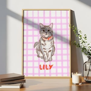 Puede incluir: Una impresión artística enmarcada con una ilustración en acuarela de un gato gris y blanco con un collar rojo, sobre un fondo a cuadros rosa y blanco. El nombre "LILY" está escrito en rojo debajo.