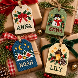 May include: Four rectangular cross-stitch gift tags featuring holiday designs and names. One tag is cream with holly and 'ANNA', one is green with a snowman and 'EMMA', one is blue with a winter scene and 'NOAH', and one is cream with a lantern and 'LILY'.