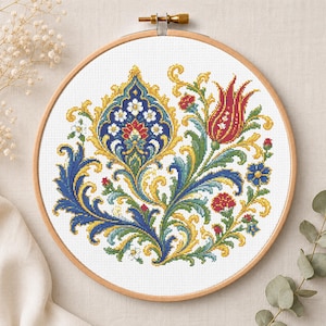 May include: A circular wooden embroidery hoop containing a white fabric panel with a cross-stitch design. The pattern features a central blue and gold floral motif, a red tulip, and intricate green, blue, and yellow scrolling leaf accents.