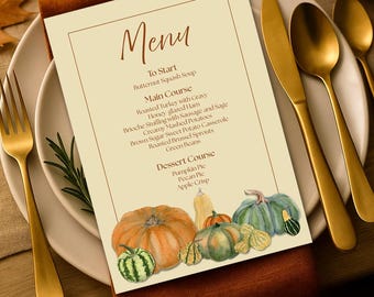 May include: A rectangular paper menu with a cream background and a thin brown border. The text lists courses including Butternut Squash Soup, Roasted Turkey, and Pumpkin Pie. The bottom features watercolour illustrations of various colourful pumpkins.