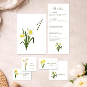 May include: A collection of white stationery with watercolor daffodil illustrations. Includes a menu, table number, and place cards. The menu lists starter, entrees, and dessert options. The place cards have names.