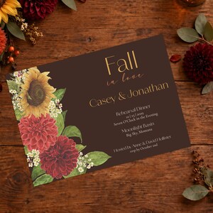 May include: A rectangular rehearsal dinner invitation card with a dark brown background. The left side features a floral arrangement of a yellow sunflower and two red dahlias with green leaves. Text reads: Fall in love, Casey & Jonathan, 10|25|2029.