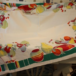 May include: A vintage white tablecloth with a colorful fruit and vegetable pattern. The border features a green stripe with vertical stripes of red, orange, yellow, and blue. The design includes red, yellow, and orange fruits and vegetables.