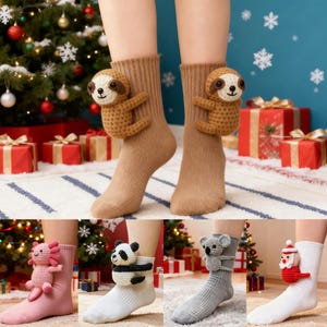 May include: A pair of brown socks with a crocheted sloth attached. The sloth is brown and tan with a smiling face. Additional socks in the image include a pink axolotl, a panda, a koala, and a Santa Claus.