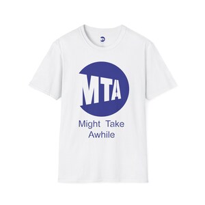 May include: White t-shirt with a blue circle graphic containing the letters "MTA" in white. Below the graphic, the text reads "Might Take Awhile" in blue. The shirt has a crew neck and short sleeves.