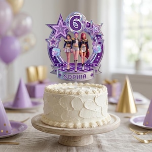 May include: A round white frosted cake topped with a purple decorative topper featuring the number 6, three stylized figures, and the name SOPHIA. The topper has a circular frame with star accents, musical notes, and a metallic purple finish.