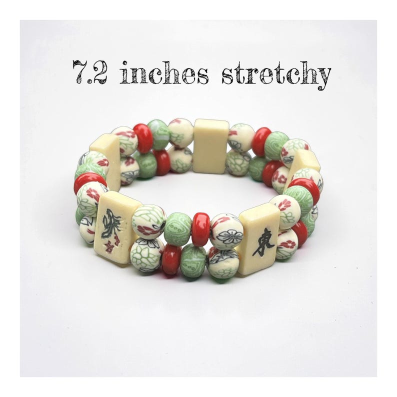 May include: A stretchy bracelet featuring cream-colored rectangular beads and round beads in red, green, and cream with floral patterns. The bracelet is approximately 7.2 inches in length. The text "7.2 inches stretchy" is above the bracelet.