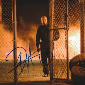 May include: A glossy photograph featuring a person in a dark shirt and trousers standing behind a chain-link fence with a large fire in the background. A sign on the left reads PRIVATE PROPERTY NO SOLICITING LOITERING TRESPASSING. A blue ink signature is visible.