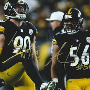 May include: A signed photograph featuring two football players in black and yellow uniforms. The player on the left wears number 90, and the player on the right wears number 56. Both athletes wear black helmets with team logos and gold accents.