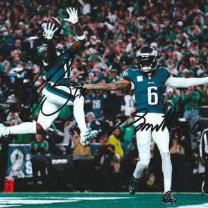 May include: A photograph captures two football players in action during a game. One player, wearing a teal and white uniform with the number 11, leaps to catch a football. The other player, in a teal and white uniform with the number 6, has his arms outstretched.