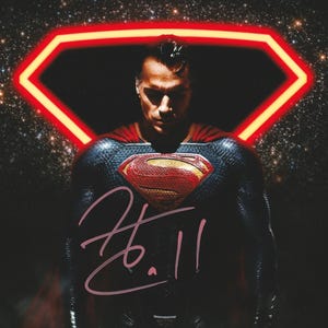 May include: A photographic print featuring a figure in a dark blue textured suit with a red and yellow chest emblem. A glowing red neon diamond shape frames the head against a starry background. A light pink handwritten signature is across the chest.