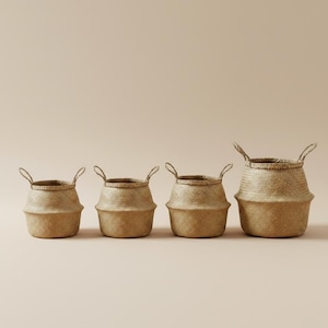 Puede incluir: Cuatro cestas de junco tejido de diferentes tamaños, cada una con asas en forma de lazo. Las cestas son de color marrón claro natural y tienen un aspecto texturizado. Las cestas están dispuestas en fila sobre un fondo neutro.