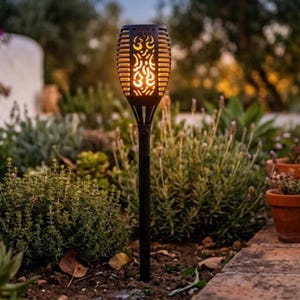 May include: A black solar-powered garden torch light with a textured, flame-shaped head featuring intricate cutouts that emit a warm, glowing light. The light is mounted on a slender, straight black stake designed for insertion into the ground.