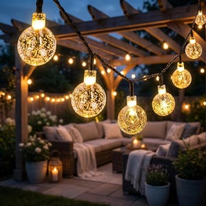 Peut inclure: Une guirlande lumineuse composée d'ampoules sphériques en verre texturé à effet bulles. Chaque ampoule diffuse une lumière dorée et chaleureuse, suspendue à un câble sombre. Les lumières sont disposées en série pour un éclairage décoratif.