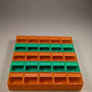 May include: A storage organizer with a grid of small, open-top bins. The bins alternate between orange and green, arranged in rows and columns. The organizer is made of plastic and is designed for small items.