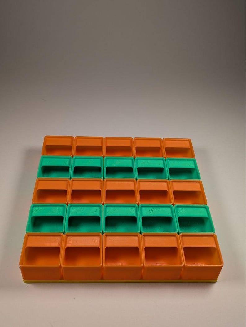 May include: A storage organizer with a grid of small, open-top bins. The bins alternate between orange and green, arranged in rows and columns. The organizer is made of plastic and is designed for small items.