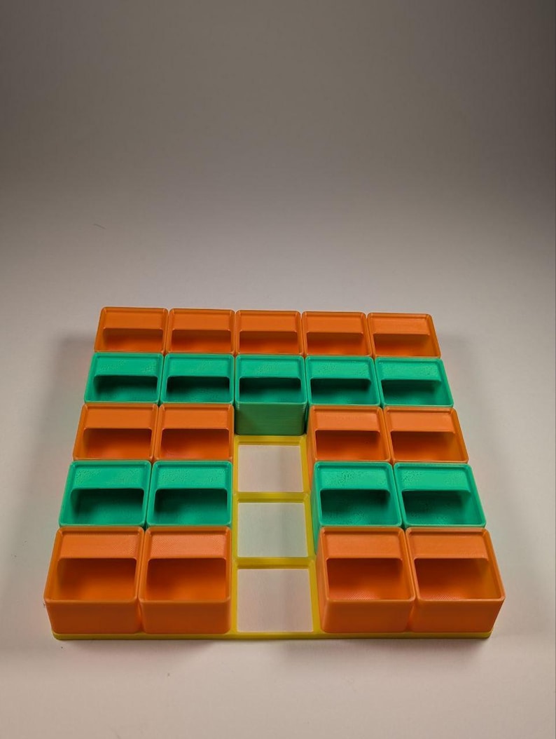 May include: A colorful storage organizer with a grid of small, square compartments. The compartments are orange, green, and yellow, arranged in a geometric pattern. The organizer is made of plastic and is designed for small items.