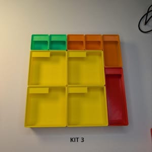 May include: A collection of colorful plastic storage containers. The set includes small green and orange rectangular boxes, along with larger yellow and red rectangular trays. The text "KIT 3" is visible at the bottom.