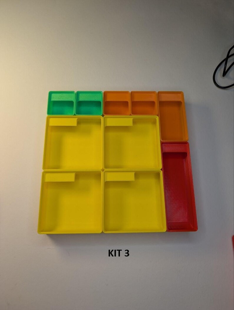 May include: A collection of colorful plastic storage containers. The set includes small green and orange rectangular boxes, along with larger yellow and red rectangular trays. The text "KIT 3" is visible at the bottom.