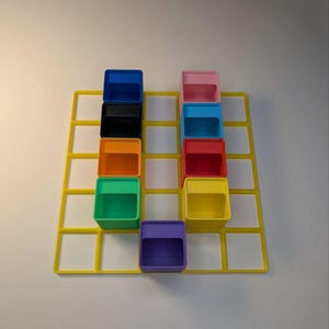 May include: A yellow grid with nine colorful, open-top boxes arranged in a 3x3 pattern. The boxes are blue, black, orange, green, purple, pink, light blue, red, and yellow. The background is white.