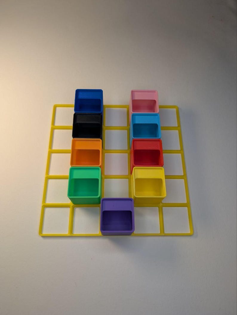 May include: A yellow grid with nine colorful, open-top boxes arranged in a 3x3 pattern. The boxes are blue, black, orange, green, purple, pink, light blue, red, and yellow. The background is white.