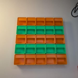 May include: A grid of twenty-four small, square, plastic containers. The containers alternate between orange and green, arranged in a pattern of four rows and six columns. The containers are empty and have a simple, open design.