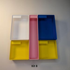 May include: A collection of colorful rectangular storage containers. The containers are in various colors, including white, pink, blue, and yellow. The text "Kit 8" is printed at the bottom of the image.