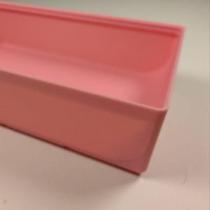 May include: A rectangular, light pink plastic container with rounded corners. The container is empty and appears to be a tray or storage box. The color is a soft, pastel pink.