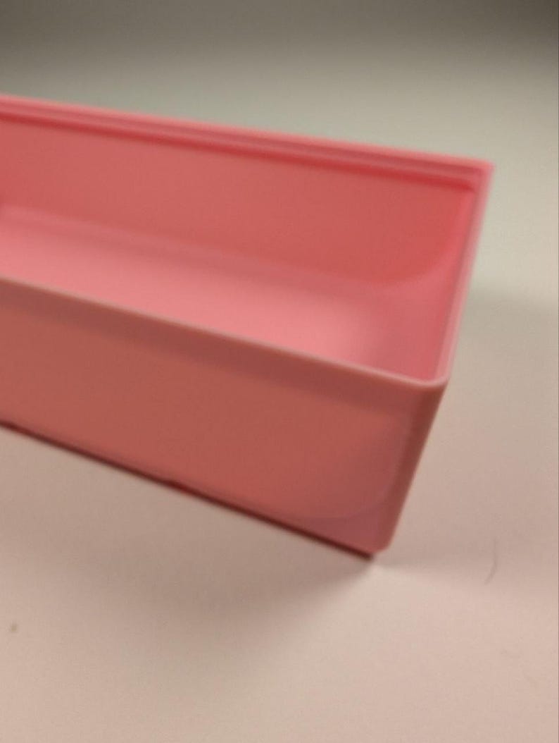 May include: A rectangular, light pink plastic container with rounded corners. The container is empty and appears to be a tray or storage box. The color is a soft, pastel pink.