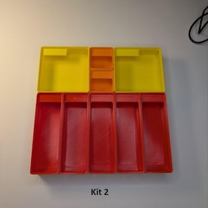 May include: A set of colorful plastic storage containers. The set includes yellow and orange square containers on top, and red rectangular containers below. The text "Kit 2" is printed at the bottom.