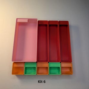 May include: A collection of colorful plastic containers. The set includes a large translucent pink rectangular box, three red rectangular boxes, and four smaller boxes in orange and green. The text "Kit 6" is printed below the containers.