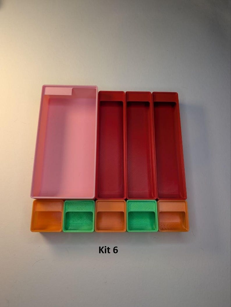May include: A collection of colorful plastic containers. The set includes a large translucent pink rectangular box, three red rectangular boxes, and four smaller boxes in orange and green. The text "Kit 6" is printed below the containers.