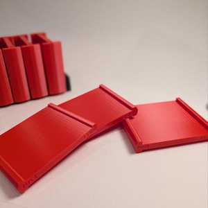 May include: A set of bright red plastic measuring gauges with flat rectangular surfaces and raised edges. Each piece features embossed text indicating specific measurements, including 2mm, 1.5mm, and 4mm, clearly visible on the side of the components.